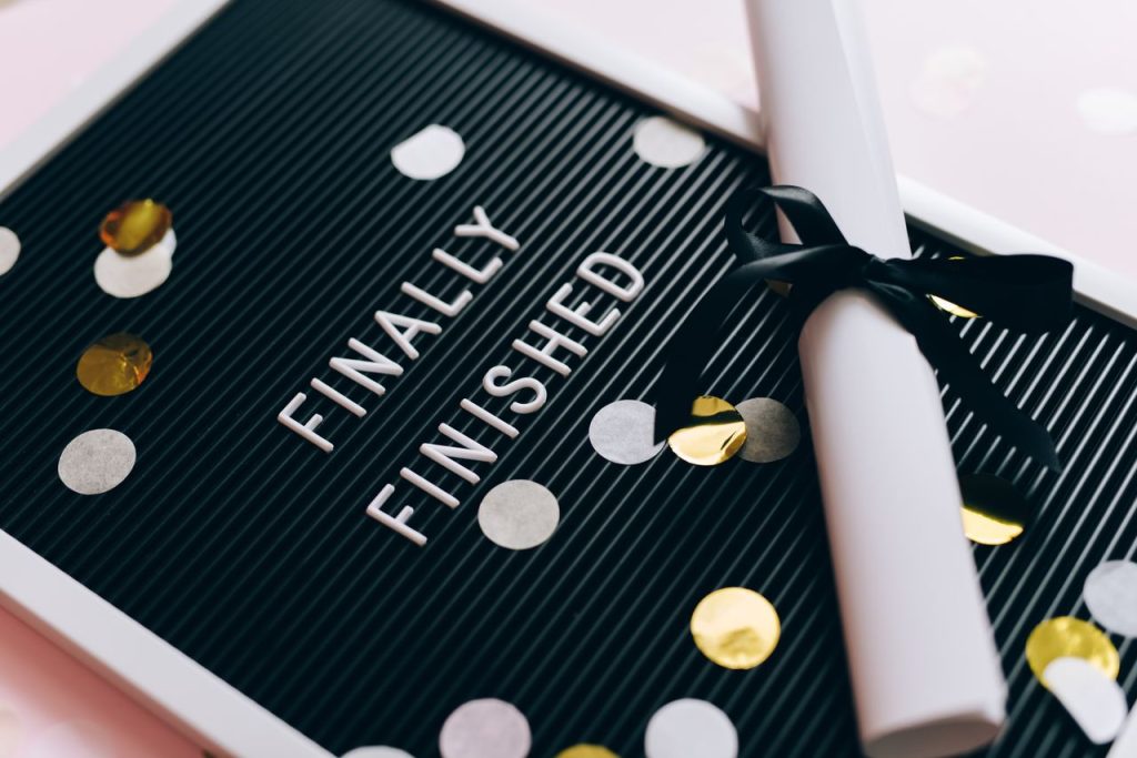 Close-up of a graduation diploma and letter board with "Finally Finished," surrounded by confetti.